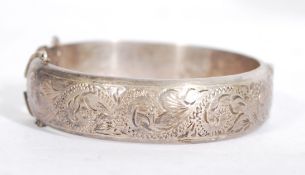 A silver hallmarked rococo chase decorated bangle with clip clasp and safety chain. Hallmarked for