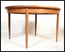A mid 20th century G-Plan teak circular pull out extending dining table with a single additional