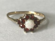 A hallmarked 9ct gold opal and garnet cluster ring. The central round cut opal having a halo of