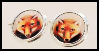 A pair of silver cufflinks with enamel panels featuring foxes. The cufflinks have a chain link