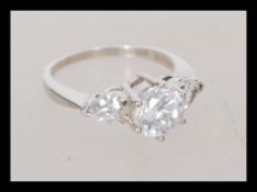 A hallmarked 9ct white gold three stone ring having a central brilliant cut stone flanked by heart