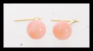 A pair of contemporary gold stud earrings with mounted coral stones.