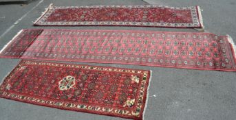 A set of three 20th century runner floor carpet rugs with red ground and geometric patterning. The
