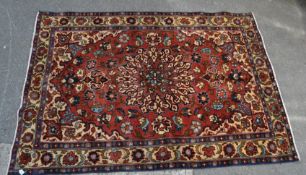 A vintage 20th century floor carpet with red ground having a central panel with a floral medallion