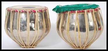 A pair of 20th Century Indian Tabla drums, polished metal casing, with hide tops. Measures 27 cm