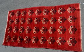 A red ground tasseled 20th century carpet floor rug. This rug includes a floral black and cream