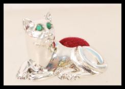 A contemporary silver pin cushion in the form of a cat with emerald eyes. In the manner of Adie