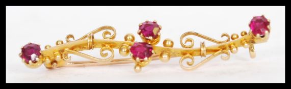 A 19th century 18ct gold Victorian bar brooch with four inset red stones. The brooch includes scroll