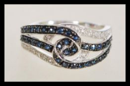 A 14ct white gold cross over split shank ring with channel set blue stones and white stones size N.