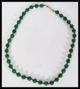 A Chinese green jade bead necklace having small gilt bead spacers with yellow metal claw clasp.