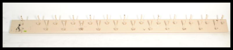 A large vintage school coat rack having a long wooden back with 24 cast metal shaped hooks. Please
