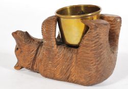 A vintage 20th century German blackforest carved wooden bear modeled on his back holding a brass