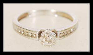 A hallmarked 9ct white gold and diamond cluster ring with channel set shoulders and a cluster