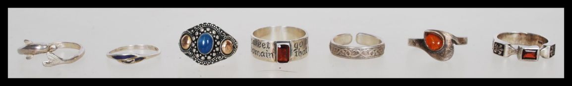A collection of seven silver rings to include a think band ring with an engraved slogan and red