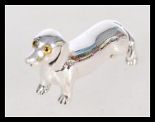 A vintage 20th century silver dog miniature figurine of a dachshund with yellow glass eyes.