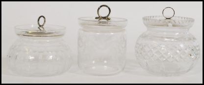 A group of three silver hallmarked lidded cut glass pots of bulbous form. The silver lids having