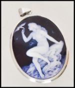 A vintage silver and enamel necklace pendant depicting a nude maiden seated on a rock holding a
