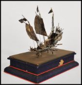 A Chinese silver model of a boat set onto a blue fabric pedestal base. Measures 15cm-high 16cm-wide.