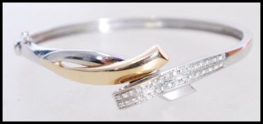 A stamped 585 white gold bangle bracelet with a cross over design having inlaid diamonds, and a