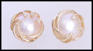 A pair of pearl earrings set into a gold decorative twisted setting with three inlaid diamonds.