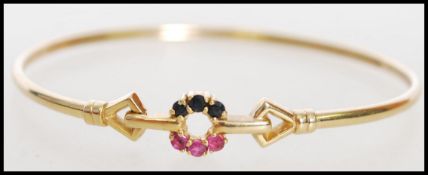 A hallmarked 9ct gold ruby and sapphire set bangle bracelet with a hook clasp. Hallmarked London.