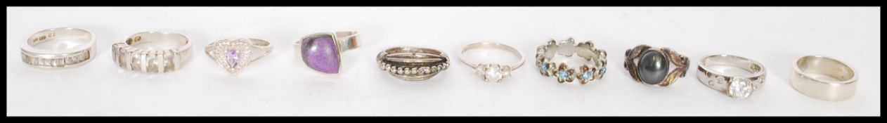 A selection of silver rings to include a heart form ring with inset purple stone, a floral ring with