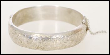 A 1980's silver bangle bracelet with a hinge opening, safety chain and floral engraving. Weight