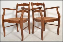 A pair of early 20th century French country oak and rattan weave fireside armchairs being raised
