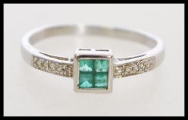A hallmarked 9ct white gold Art Deco style emerald and diamond ring set with four central square cut