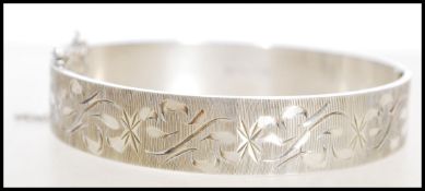 A 20th century hallmarked silver bangle bracelet with floral engraving and a hinge opening and