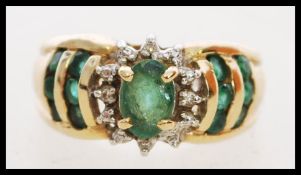 A hallmarked 14ct gold ring set with a central oval cut emerald with diamond halo having emeralds to