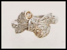 A stamped 18k white gold and diamond ring in the form of a bow with inset white and yellow diamonds.