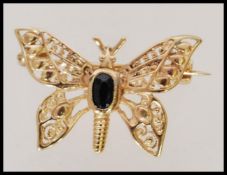 A 9ct gold brooch in the form of a butterfly with pierced detailing and central inset blue stone,