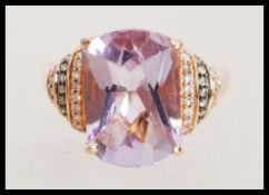 A stamped 14k rose gold ring, with a large purple stone and graduated shoulders with inset diamonds.