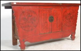 A Chinese 19th / 20th century large red lacquer sideboard of shaped form. The worn flared top over