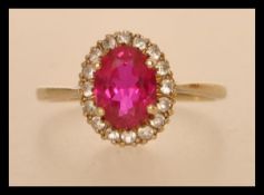A hallmarked 9ct gold ring having a large central faceted synthetic ruby surrounded by a halo of
