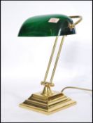 A vintage 20th century bankers desk lamp having an adjustable green glass shade raised on a brass