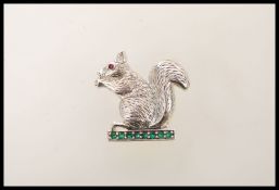 A silver brooch in the form of a squirrel set with a row of brilliant cut emeralds,having a red