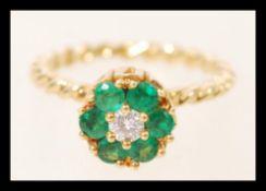 An 18ct gold twist flower head ring set with six brilliant cut emeralds around a central diamond.