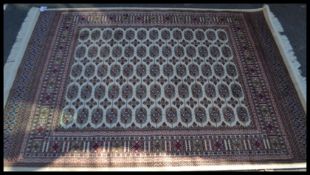 A Persian Islamic beige ground Bokhara rug with medallions to the central panel, and a red border