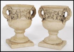 A pair of antique style white marble type composite urns raised on square bases with grape and