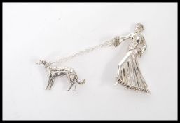 A silver Art Deco style brooch of a lady walking her dog attached by a chain having marcasite accent