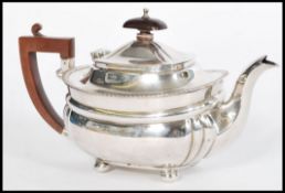 An early 20th century silver hallmarked teapot raised on bun feet with shaped wooden handle.