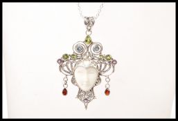 A silver necklace having a pendant in the form of a face having decorative scrollwork set with