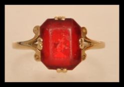 An early 20th century hallmarked 9ct gold ring set with an octagon cut red stone and scrolled