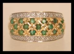 A 14ct gold diamond and emerald ring having three rows of emeralds flanked by two rows of illusion