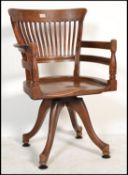 An early 20th century oak industrial office swivel captains chair raised on splayed legs with shaped