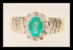 A stamped 14ct gold ring set with a central oval cut emerald and diamond accent stones to the head
