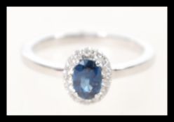 A stamped 18k white gold ring set with an oval cut central sapphire having a halo of diamonds.