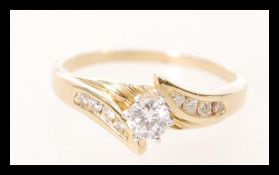 A ladies gold serpentine ring prong set with a brilliant cut diamond with further diamond accent